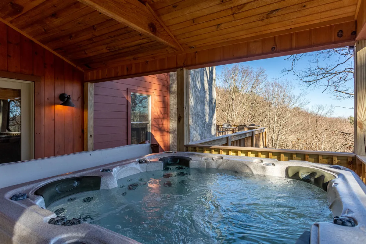 A tranquil scene featuring a hot tub on a spacious wooden deck, surrounded by lush nature. The deck is securely gated, with plenty of room for dogs to move around safely. The deck provides sweeping mountain views and is ideal for relaxing or enjoying outdoor activities with pets.