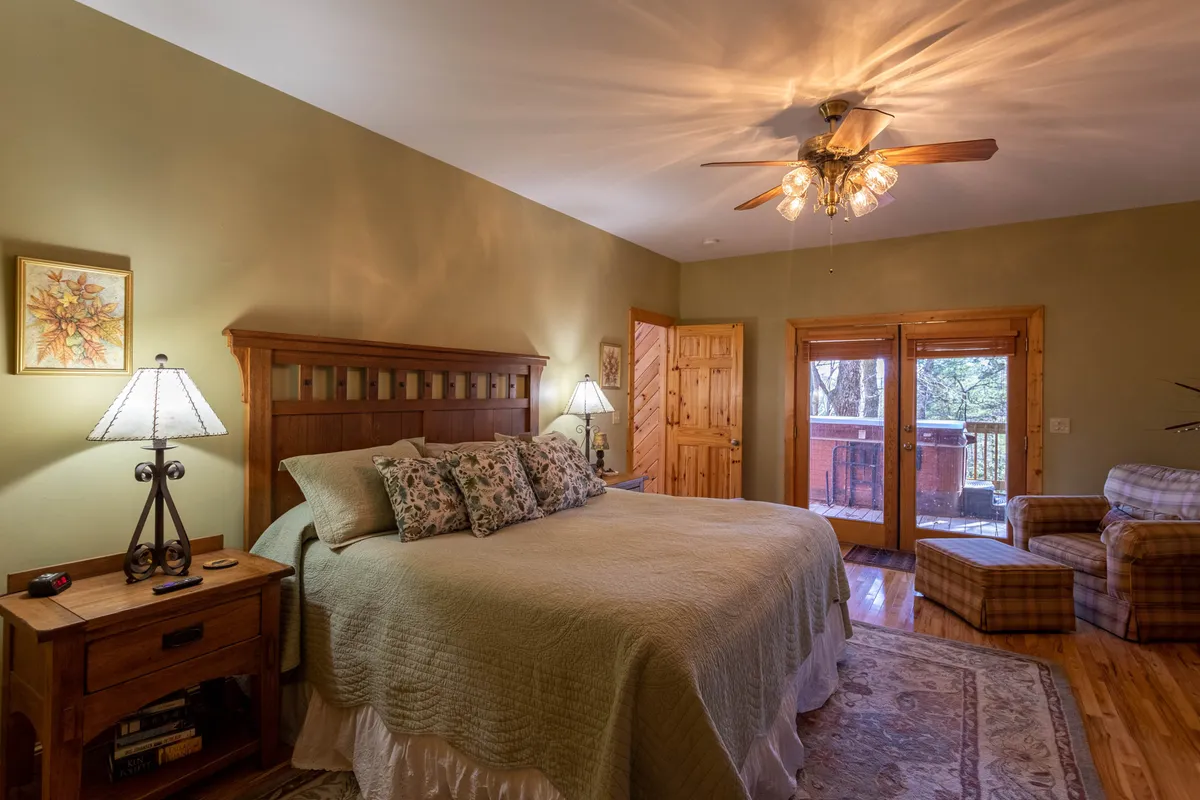 A serene bedroom setting with a comfortable bed, bedside lamps, an armchair, and a window letting in natural light. The arrangement creates a peaceful environment ideal for winding down.