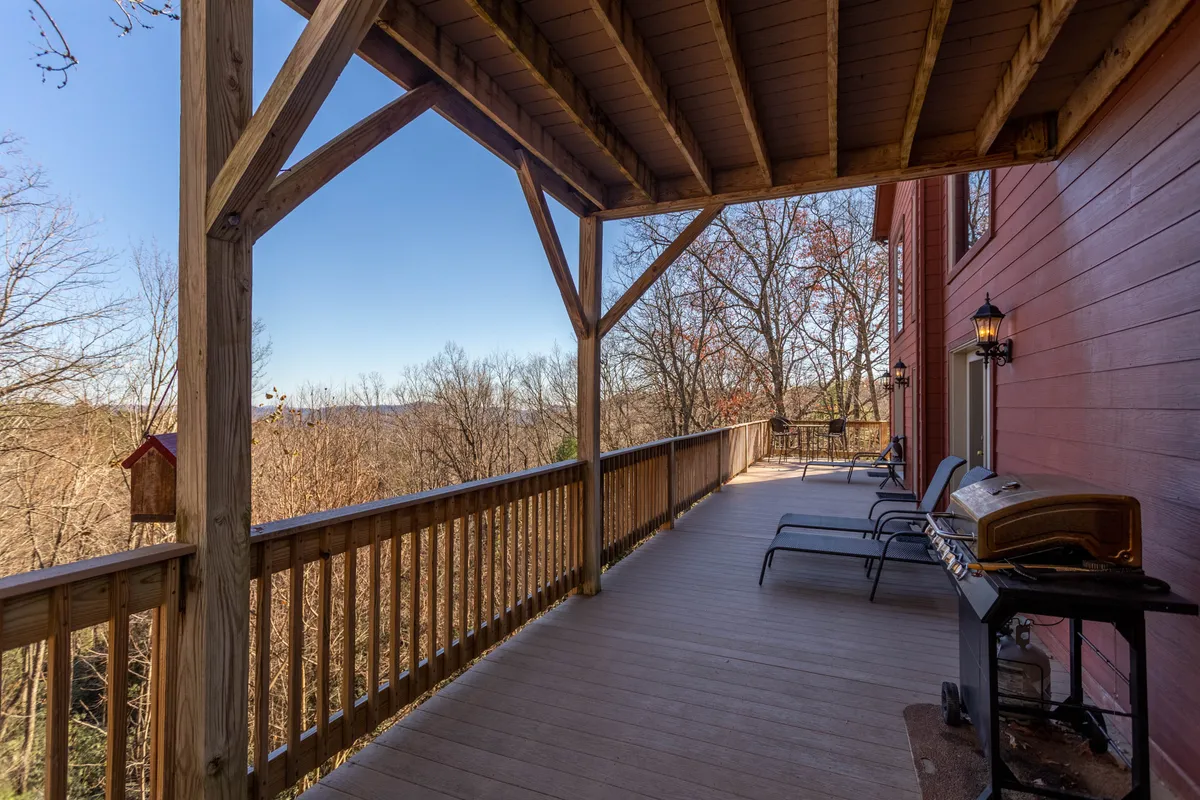 Showing a scenic wooden deck with sturdy railings, deck chairs arranged for relaxation, a gas grill ready for outdoor cooking, and a sweeping mountain view beyond. The overall feel is peaceful and perfect for social gatherings or family meals.