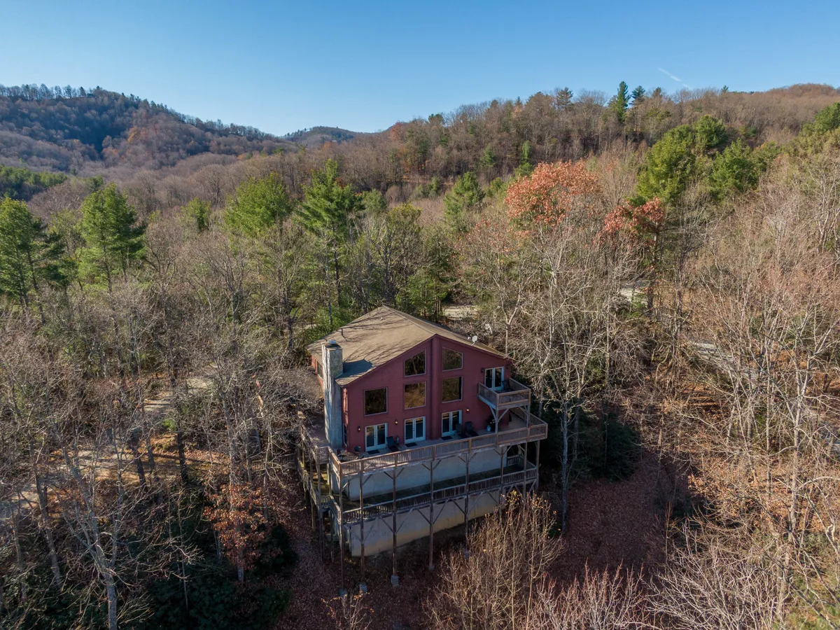 The image shows a charming cabin nestled among lush trees, set against a breathtaking mountain backdrop. The spacious deck offers sweeping sunset views, inviting guests to relax and soak in the tranquil surroundings. The natural setting hints at opportunities for hiking, wildlife watching, and stargazing.