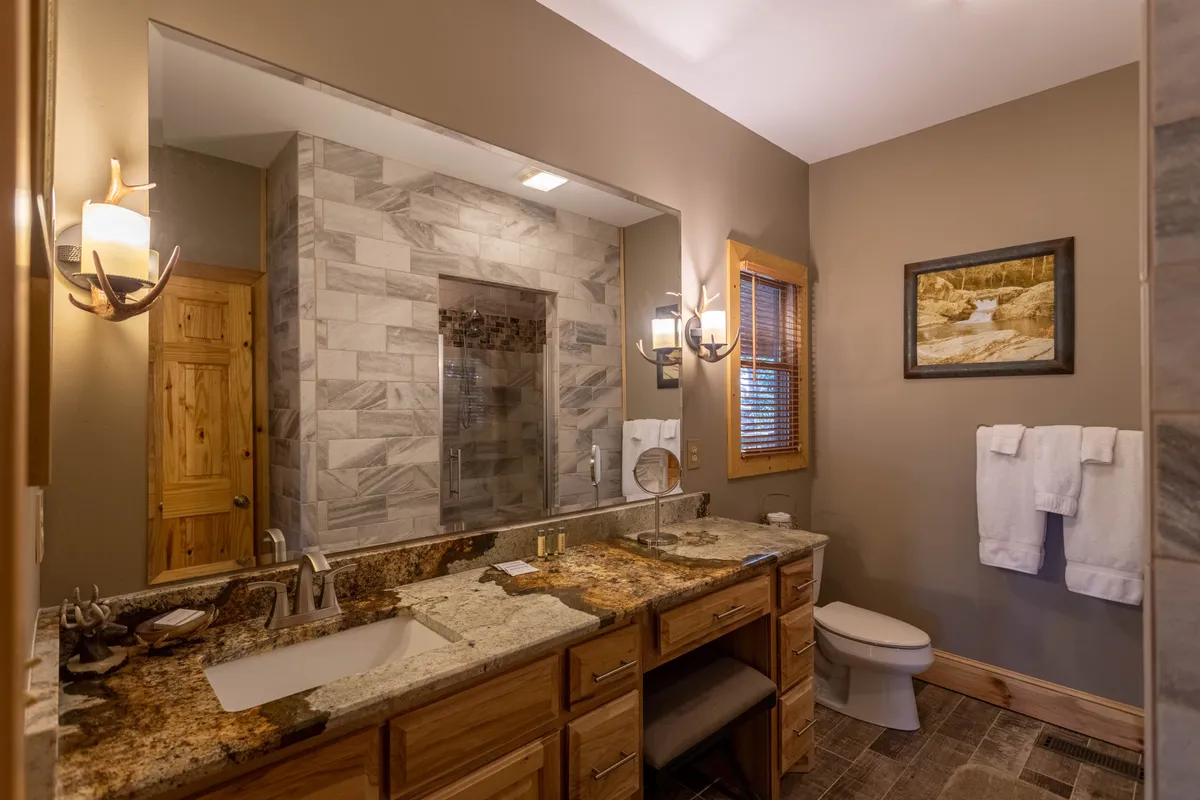 A luxurious bathroom with a granite countertop vanity, large mirror, glass-enclosed shower, and tasteful artwork creates a serene, spa-like ambiance.