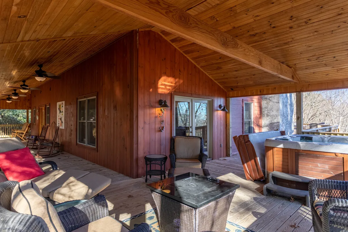 This image showcases a spacious wooden deck featuring a bubbling hot tub, comfortable rocking chairs, and inviting outdoor seating, all set against a tranquil backdrop of surrounding trees. The sunset glow enhances the sense of relaxation and highlights the deck’s positioning for optimal views.