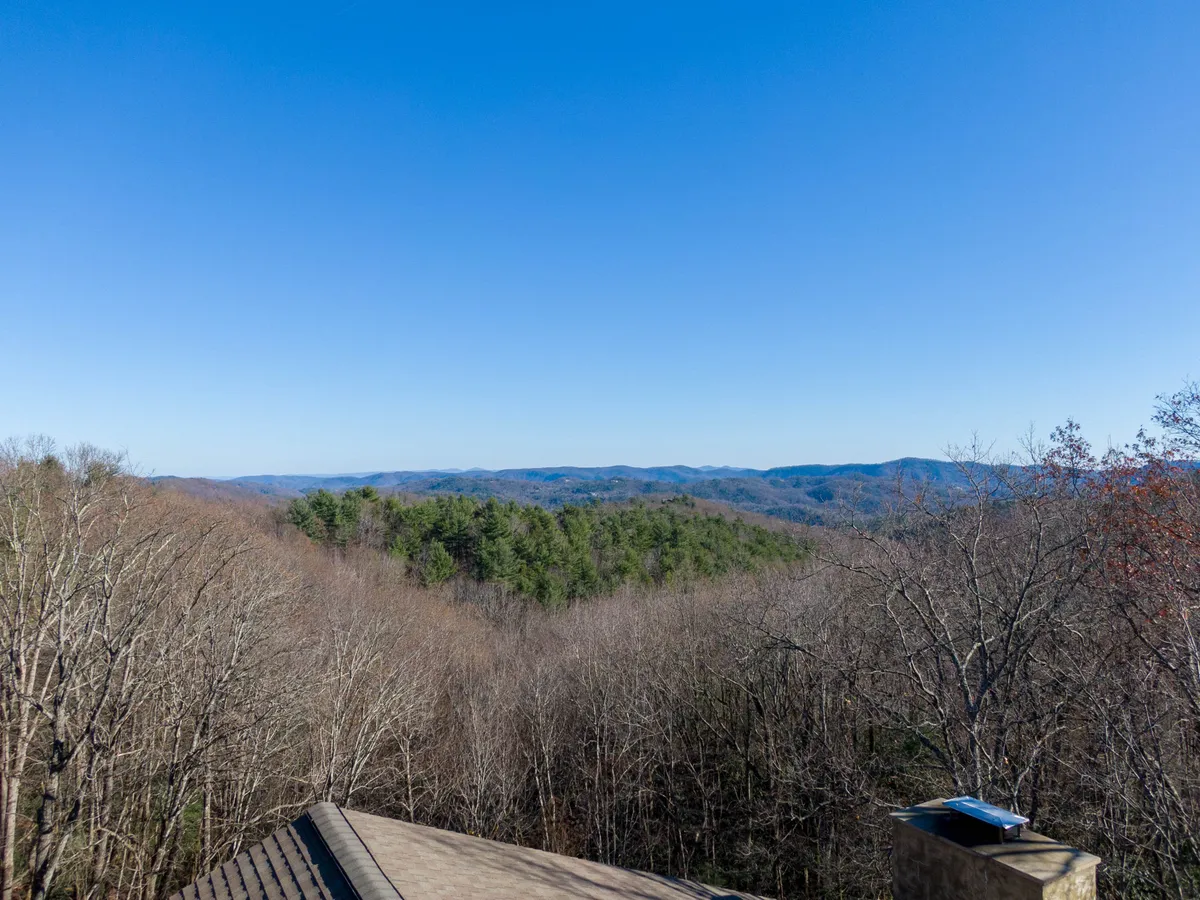 A sweeping view of the Blue Ridge mountain range with bare trees in the foreground and a clear blue sky above. The image evokes a sense of wide-open wilderness, with hints of the changing seasons visible in the landscape, making it ideal for showcasing the area's hiking and outdoor adventure opportunities.