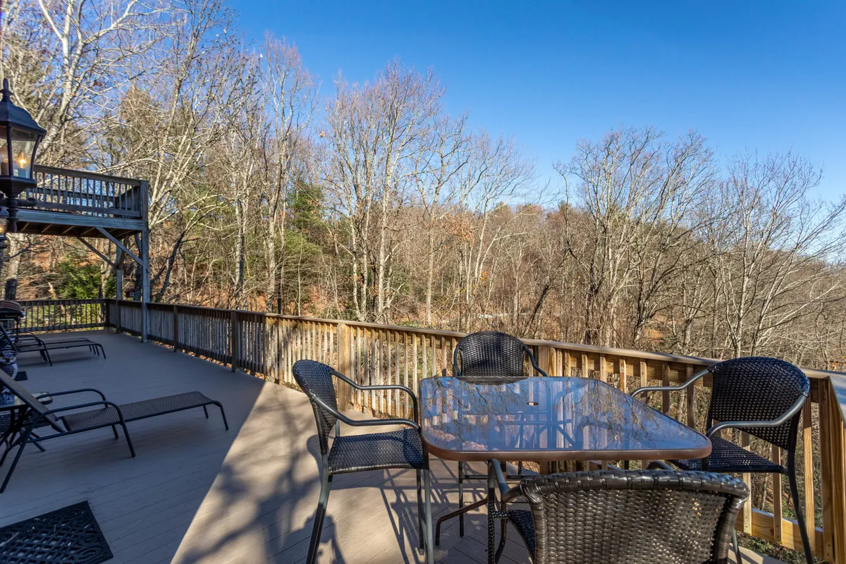 Features an outdoor dining table set on a wooden deck surrounded by trees, with lounge chairs nearby. The atmosphere is serene, ideal for enjoying meals outside or simply relaxing with loved ones.