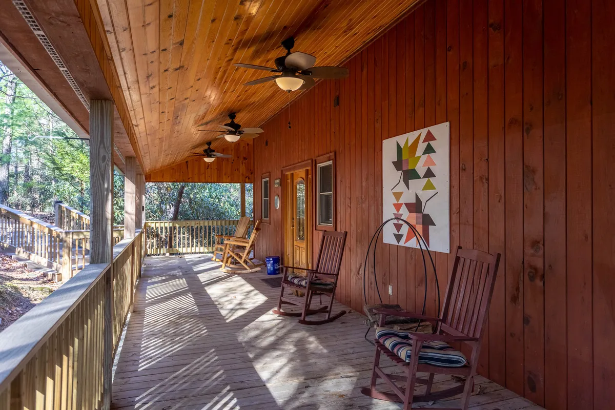 A welcoming wooden deck furnished with rocking chairs, set against a backdrop of lush greenery. The space invites guests to unwind, listen to nature, and enjoy the tranquility after a day of hiking. Ceiling fans and decorative wall art add comfort and charm.